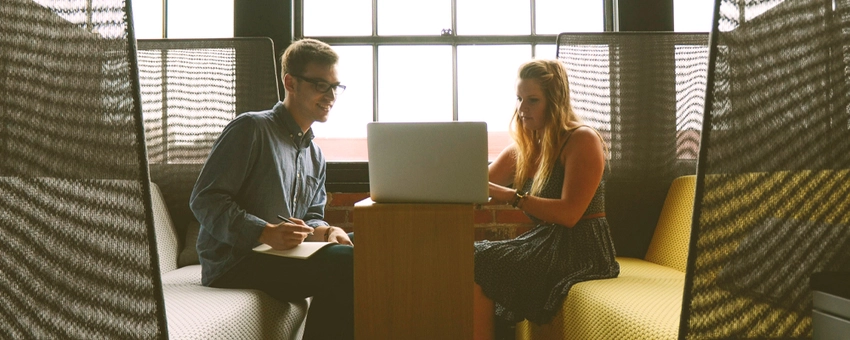 Two people collaborating on a laptop in a workspace